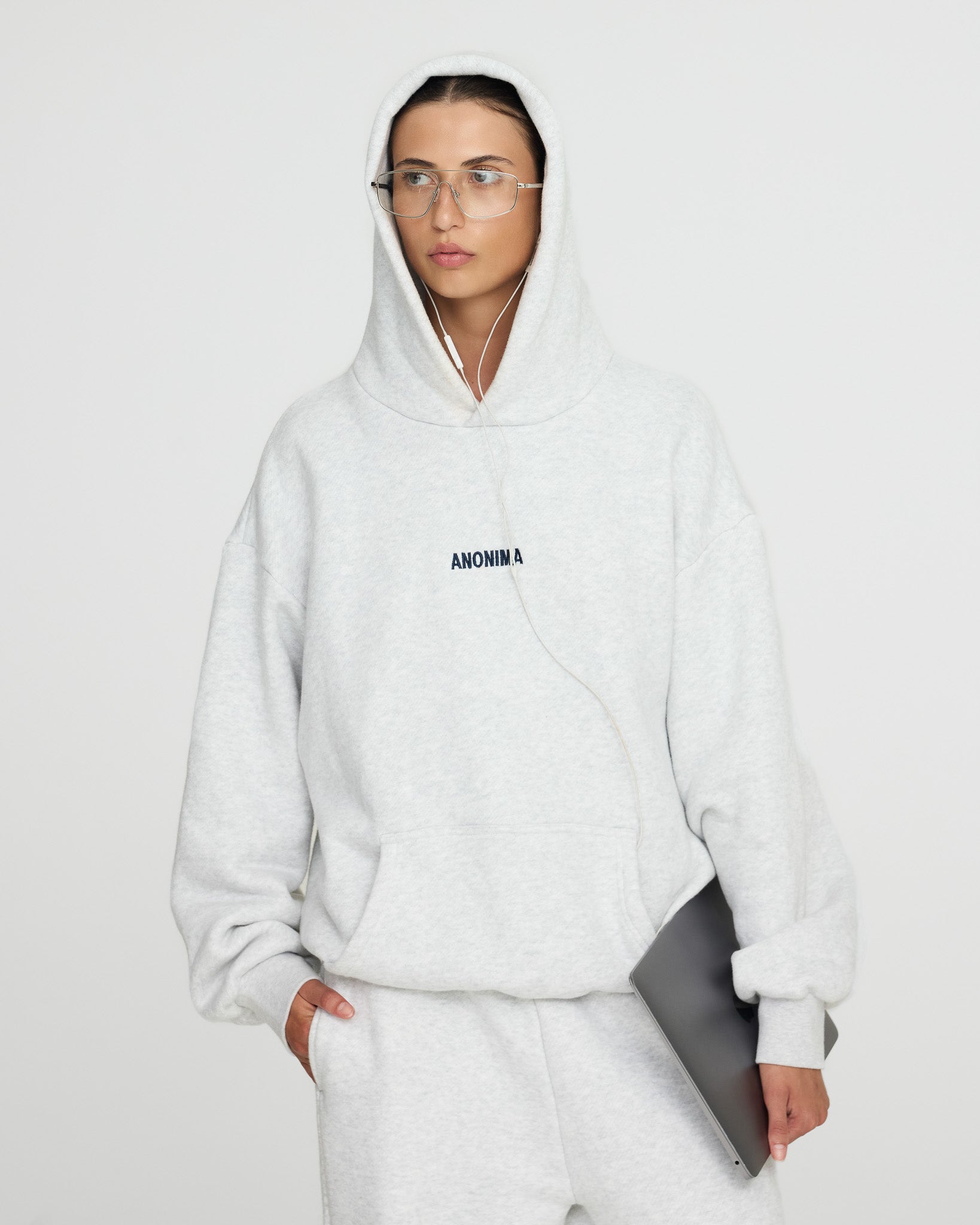 Person wearing a white hoodie with 'ANONIMA' text on a plain background