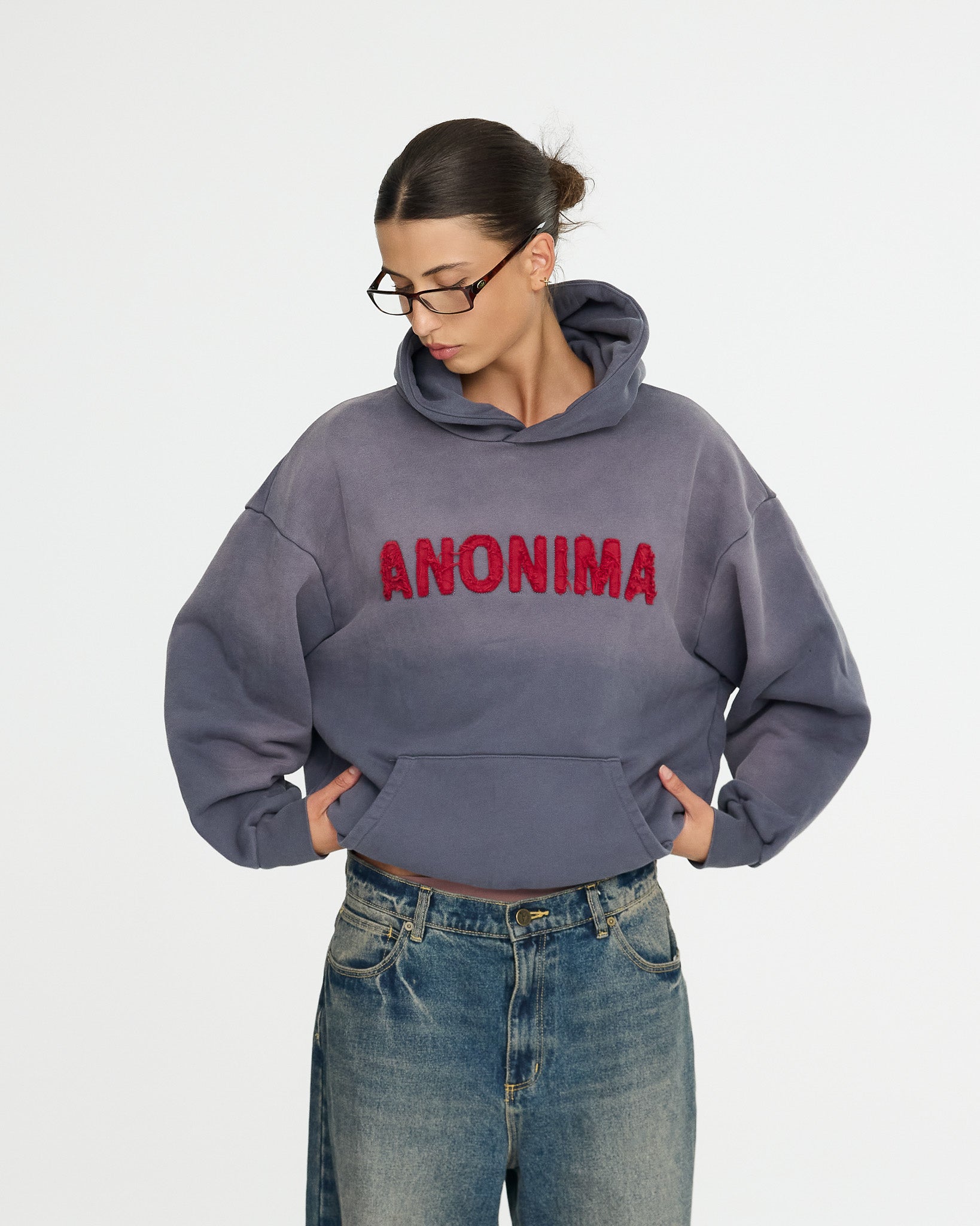 Person wearing a gray hoodie with 'ANONIMA' text on a white background