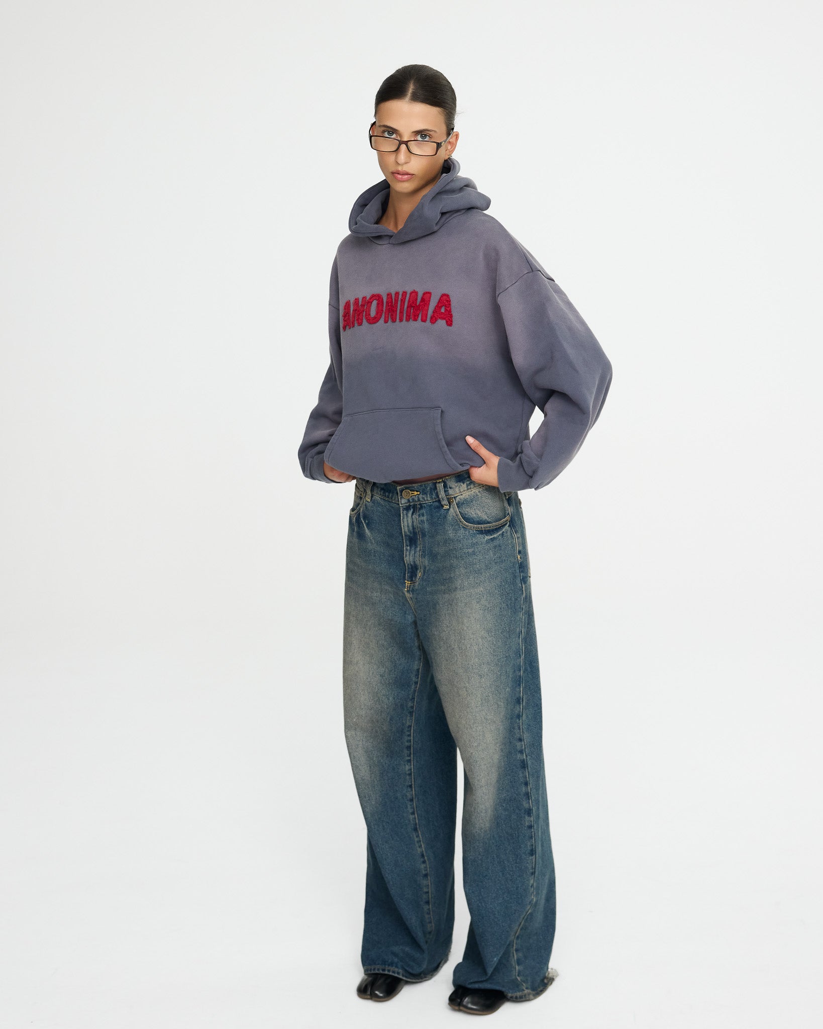 Person wearing a gray hoodie with red text and blue jeans on a white background