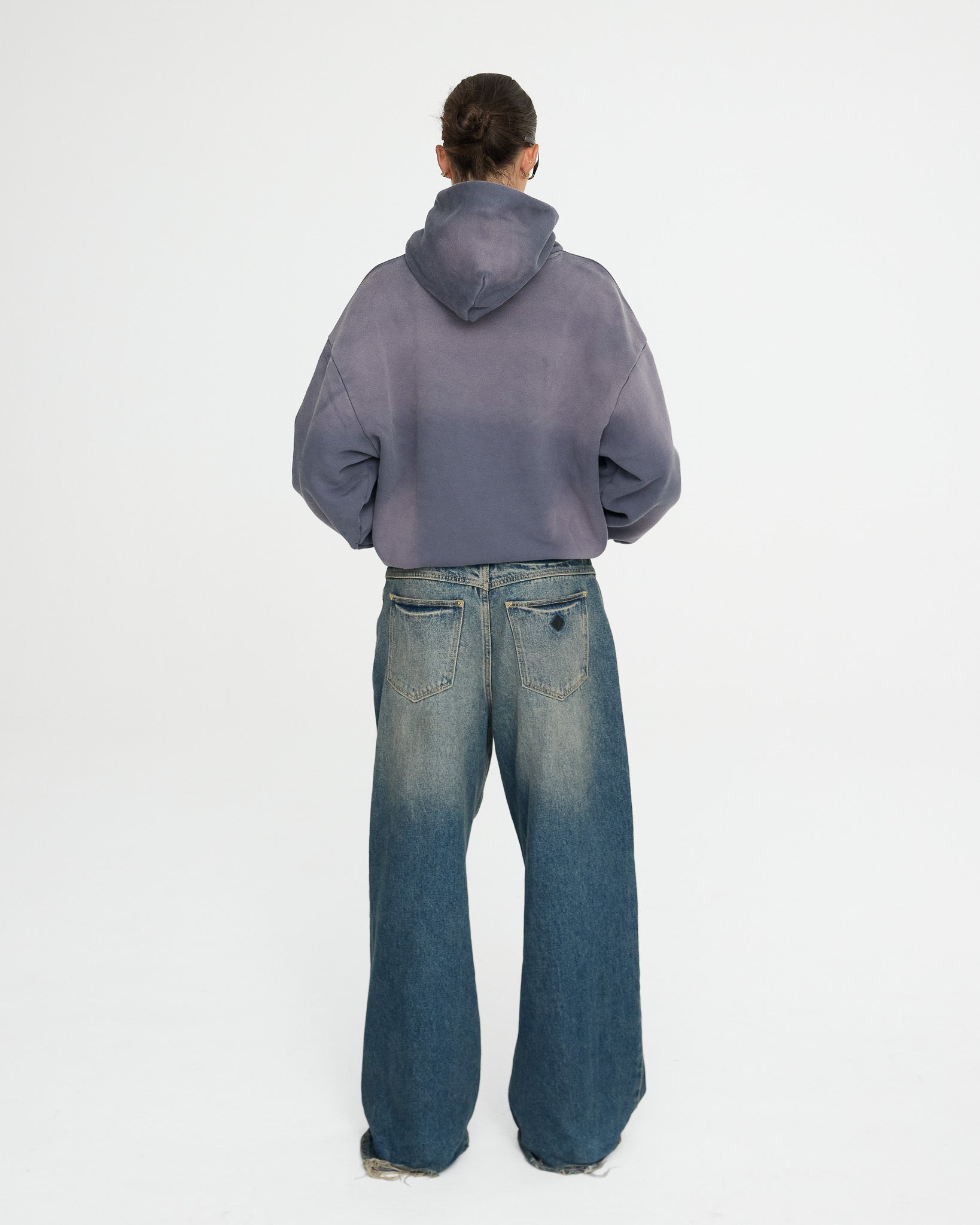 Person wearing a gray hoodie and blue jeans on a white background