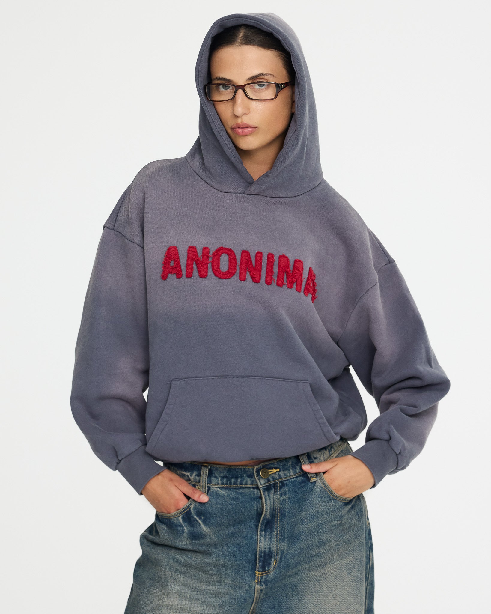 Person wearing a blue hoodie with 'ANONIMA' text on a white background