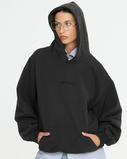 Person wearing a black hoodie with a brand logo, light blue jeans, and glasses on a white background