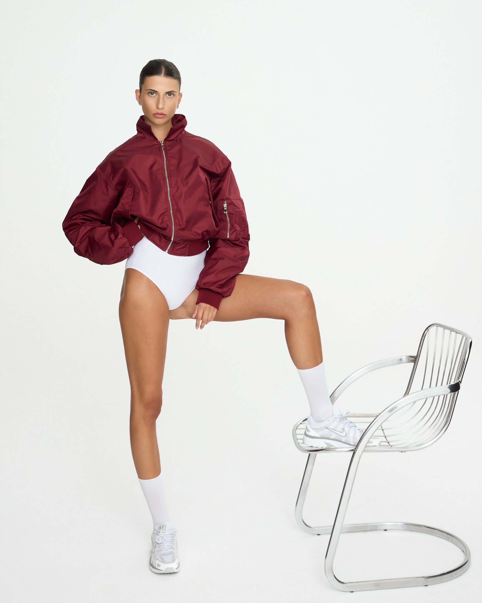 Person wearing a red jacket and white shorts sitting on a clear chair against a white background