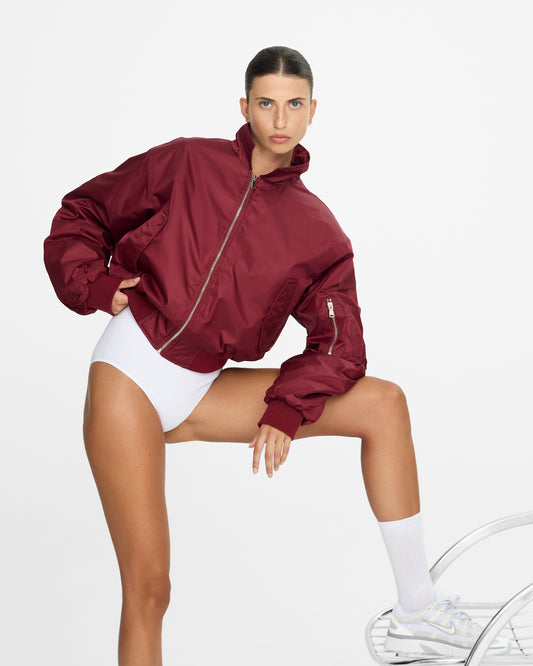 Woman wearing a maroon jacket over a white outfit on a plain background