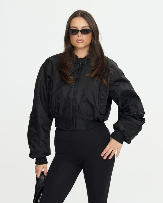 Woman wearing a black bomber jacket and sunglasses on a white background