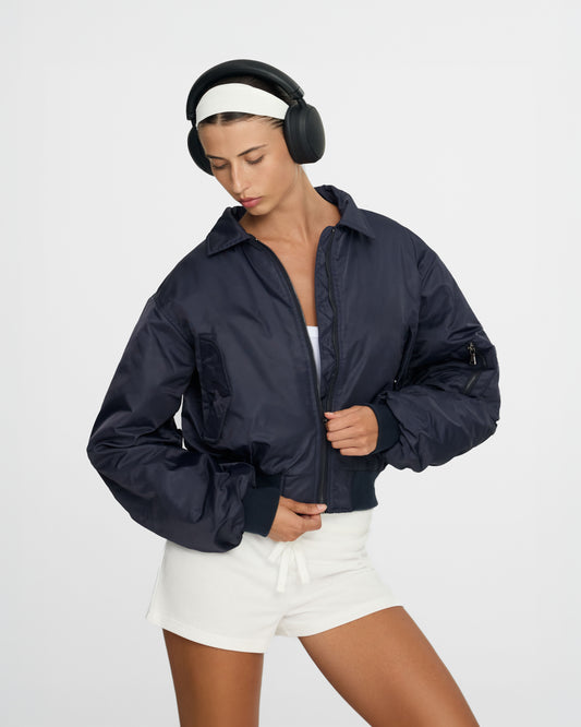 Person wearing a navy blue jacket and headphones on a light gray background