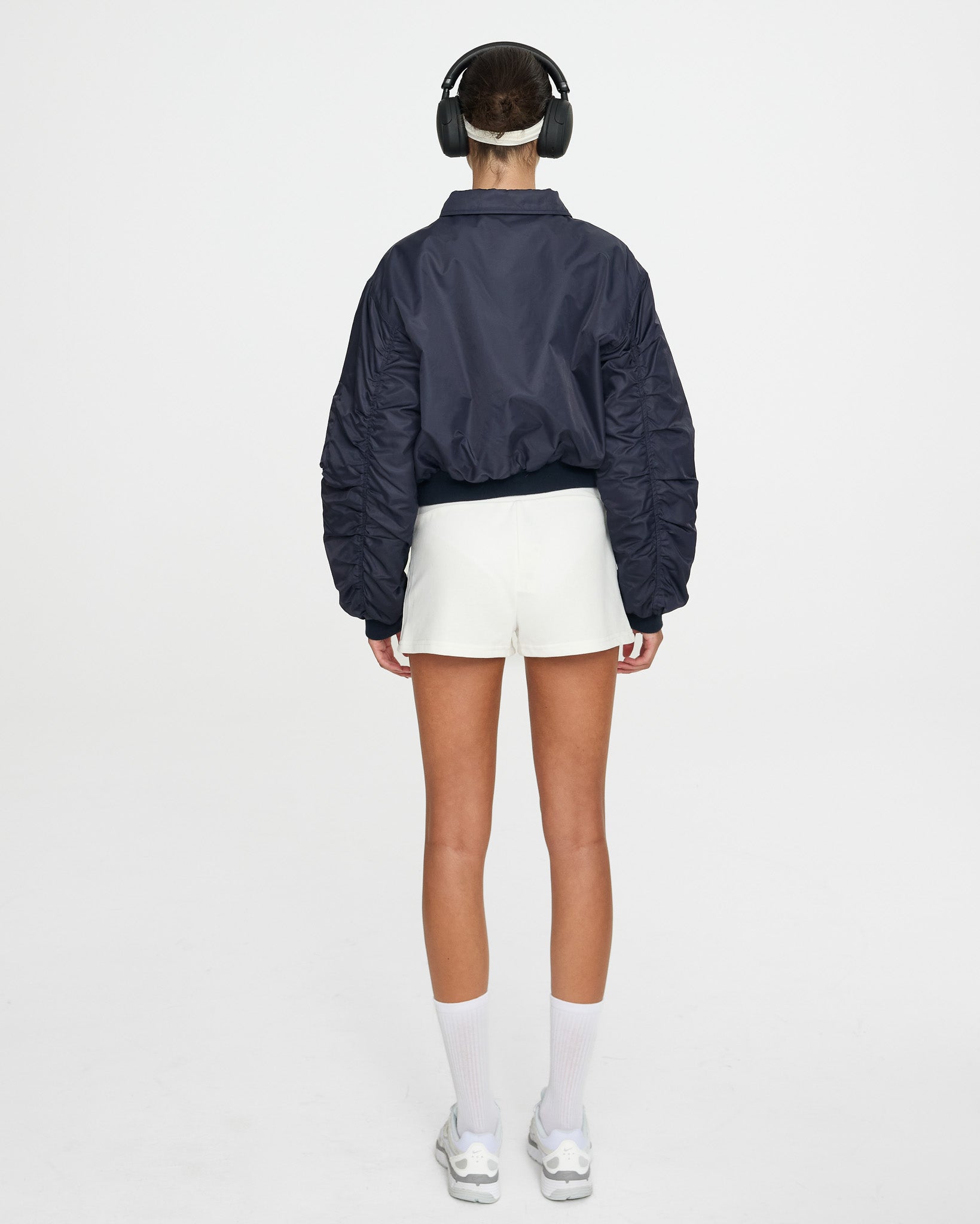 Person wearing a navy blue jacket, white shorts, and headphones on a white background