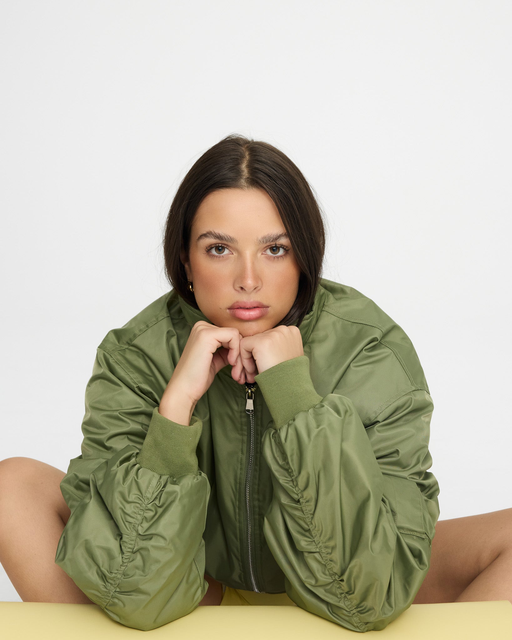 Woman wearing a green jacket sitting on a white background