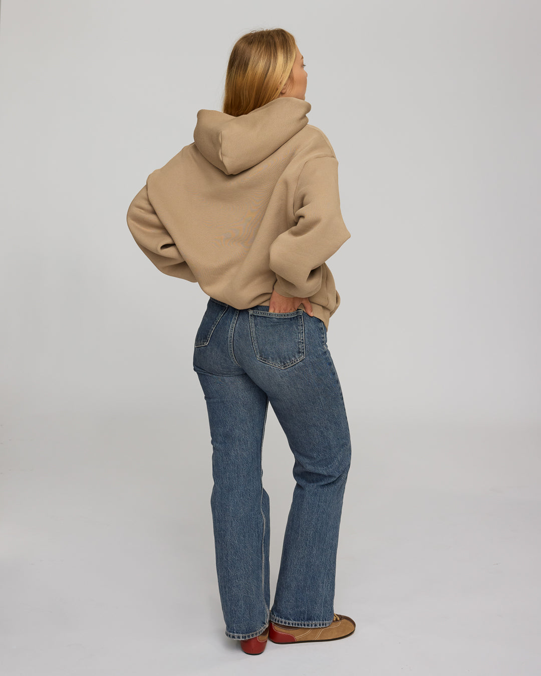 Person wearing a coffee hoodie and blue jeans on a plain background