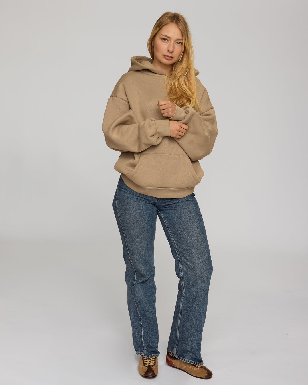 Woman wearing a coffee hoodie and blue jeans on a white background