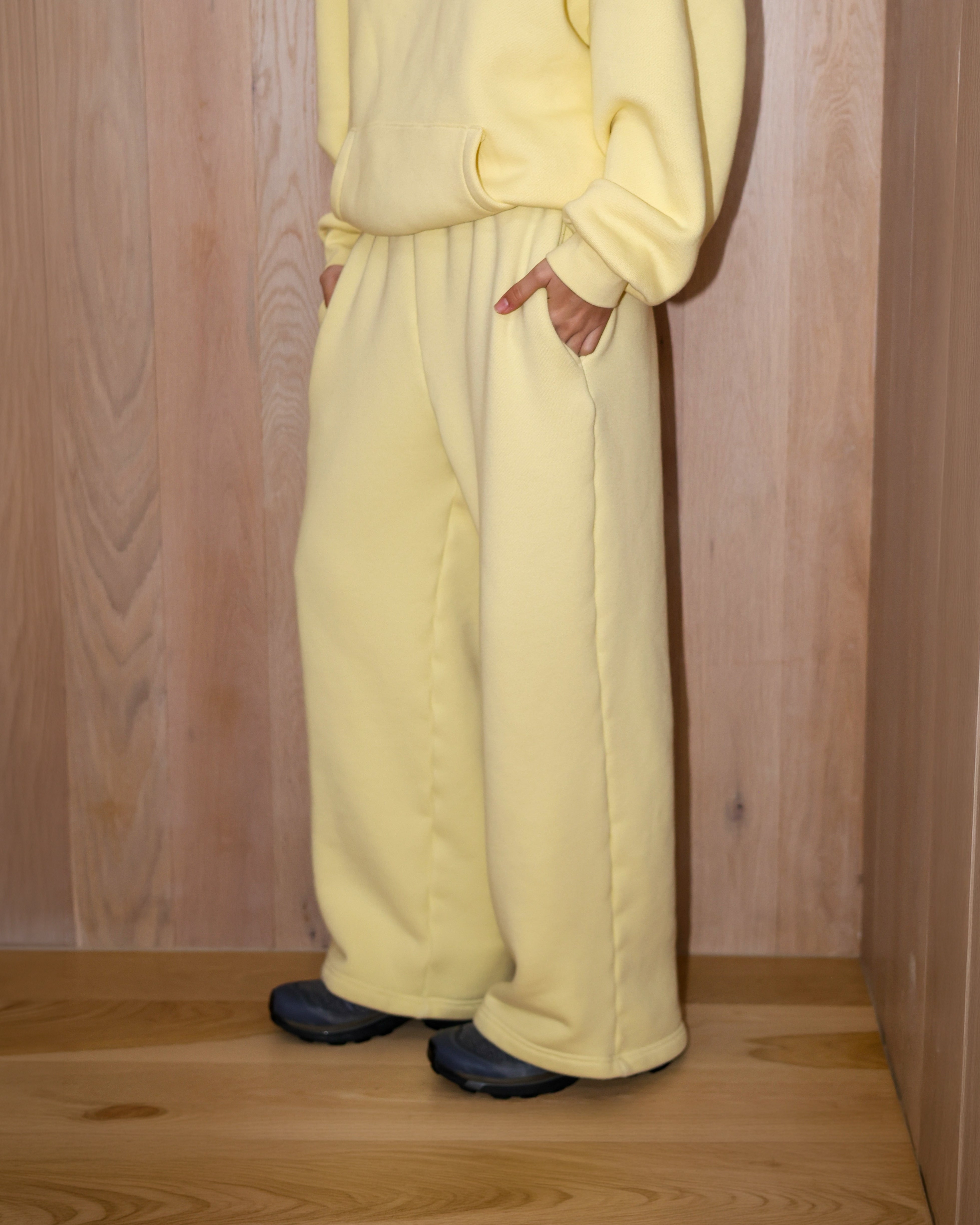Person wearing a light yellow tracksuit against a wooden paneled wall.