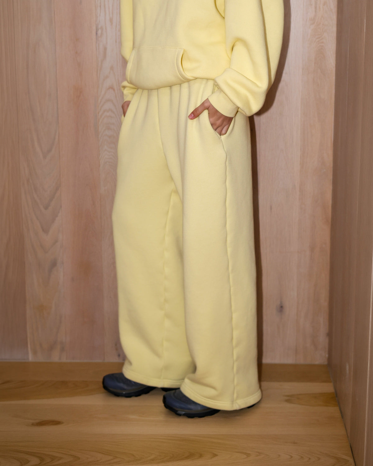 Person wearing a light yellow tracksuit against a wooden paneled wall.