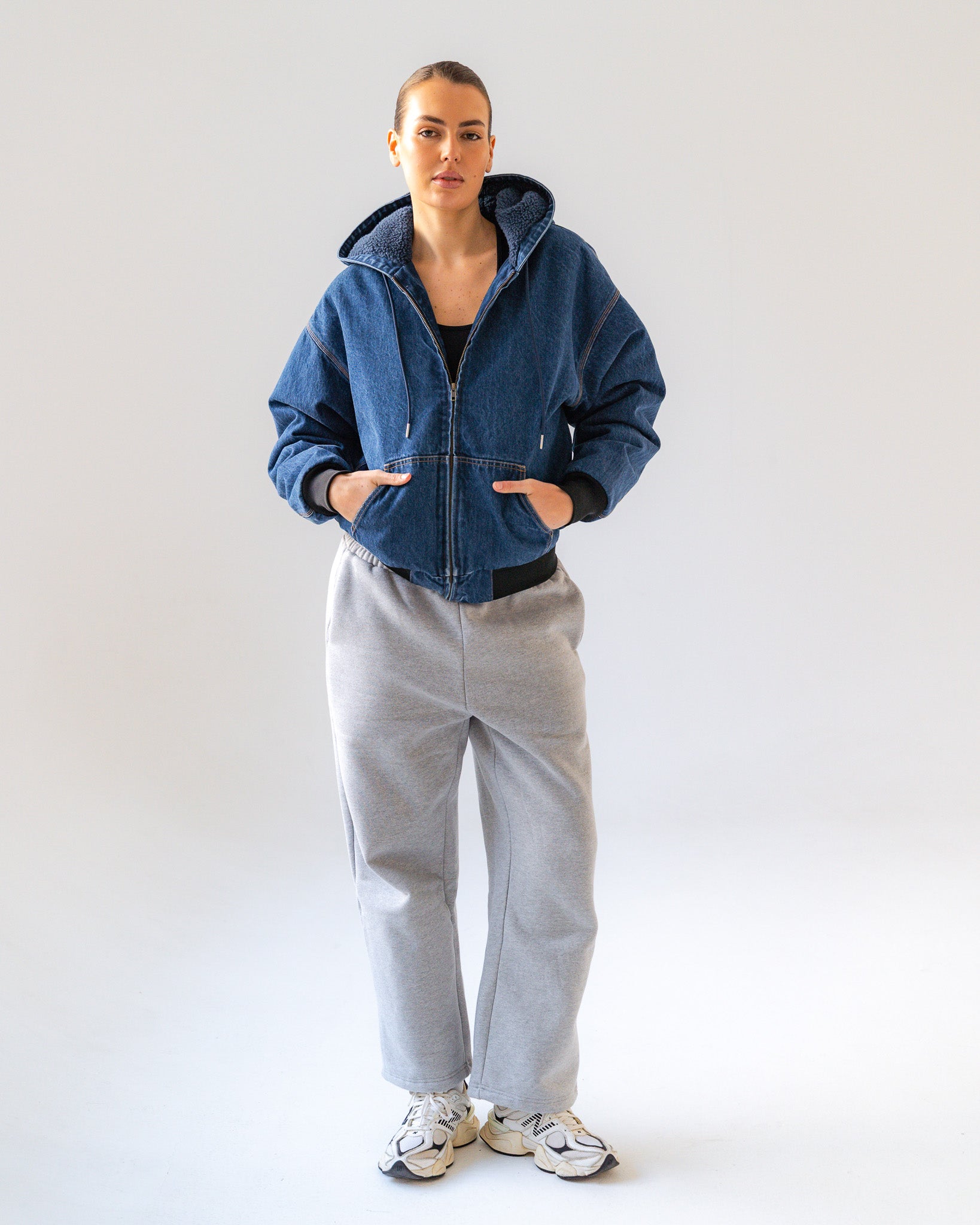 Person wearing a blue jacket and gray pants on a white background