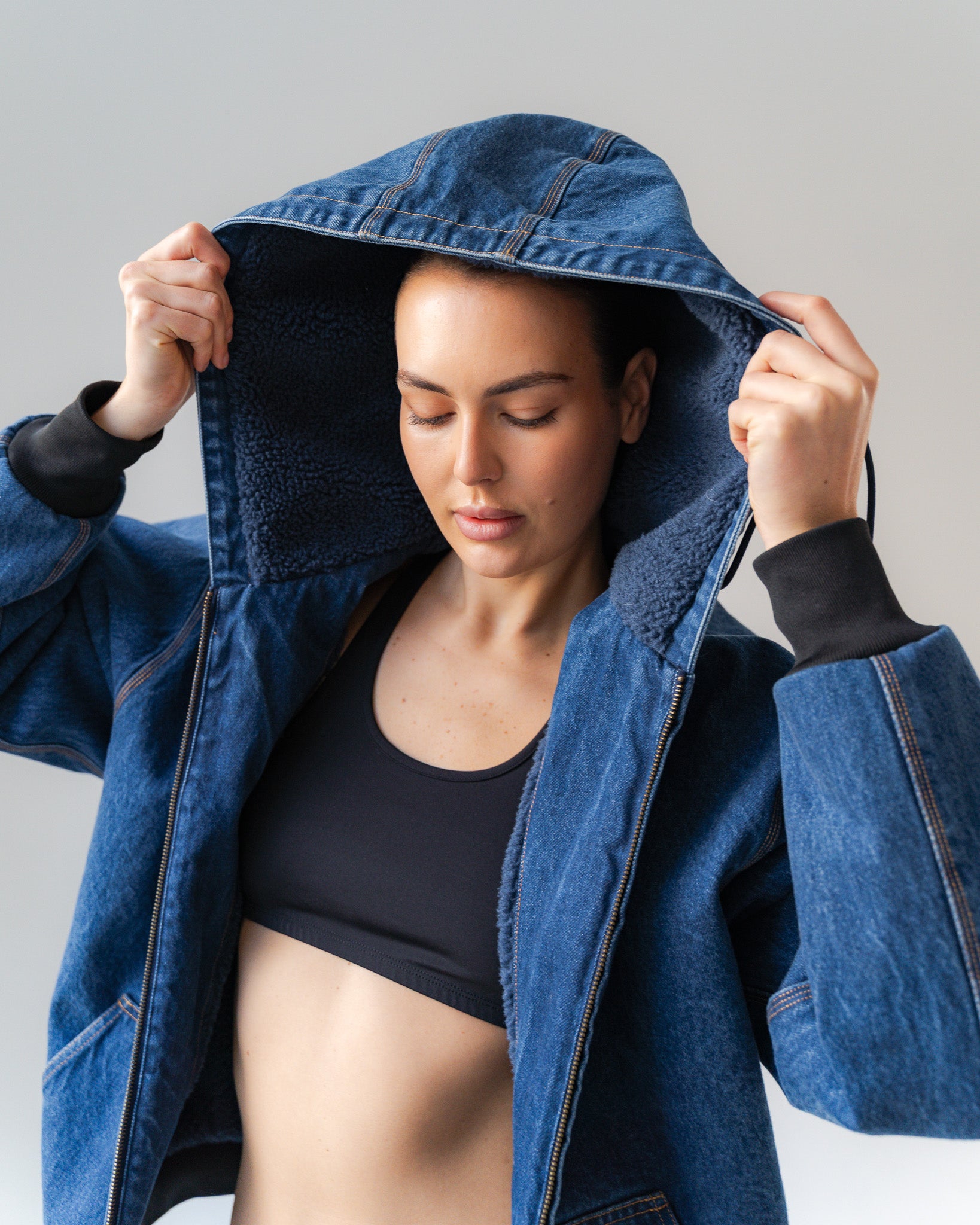 Woman wearing a blue denim jacket over a black top against a gray background